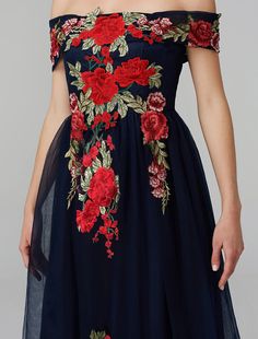 a woman wearing a dress with red flowers on it and an off the shoulder top