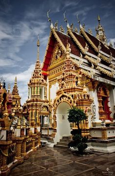 an elaborately decorated building with gold and red decorations on the roof, in front of a cloudy blue sky