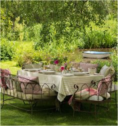 an outdoor table set up with pink and white linens in the middle of a grassy area