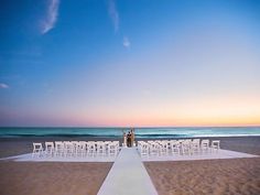 a couple standing at the end of a white aisle on top of a sandy beach