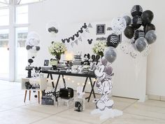 a mickey mouse party with black and white balloons on the wall, decorations and table