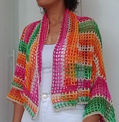 a woman wearing a colorful crochet shawl and white top standing in front of a door