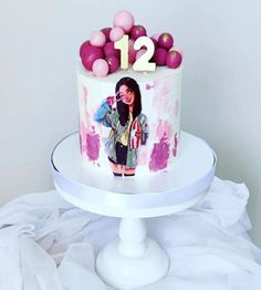 a decorated birthday cake with pink and purple balloons on the top, sitting on a white pedestal