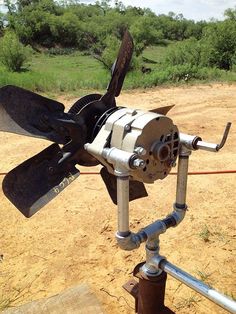 an old propeller sitting on top of a metal pole in the dirt near some trees