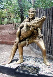 a bronze statue of a man holding an alligator in front of a fenced area