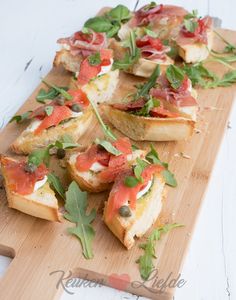 a wooden cutting board topped with slices of bread covered in toppings