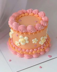 two tiered cake with pink frosting and flowers on top, sitting on a white surface