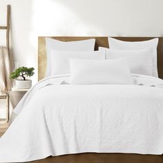 a bed with white linens and pillows in a clean bedroom area, next to a potted plant