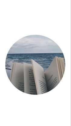 an open book sitting on top of a beach next to the ocean