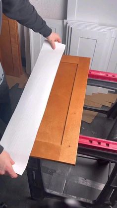 a person holding a piece of white paper over a cabinet door with red tape on it