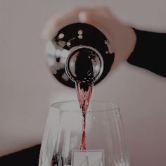 someone pours red wine into a glass in front of a white wall and black table