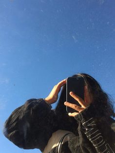 a woman taking a selfie with her phone in front of the camera and blue sky