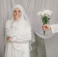 a woman in white dress holding flowers next to a man