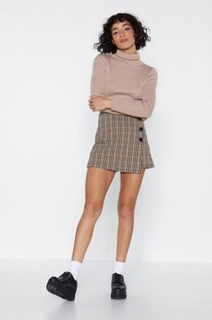 a woman in a skirt and turtle neck sweater poses for the camera with her hands on her hips