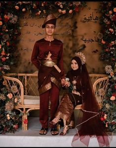 a man and woman dressed in traditional arabic garb posing for a photo with flowers on the wall behind them