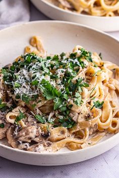 pasta with mushrooms and parmesan cheese in a white bowl on top of a table