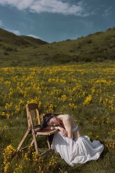 a woman in a white dress is laying on a wooden chair in a field with yellow flowers