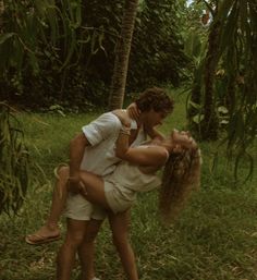 a man holding a woman in his arms while standing next to some trees and grass