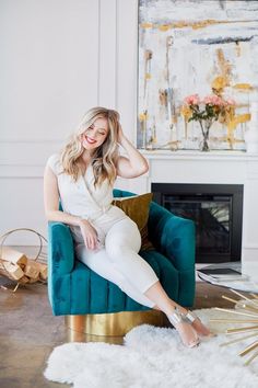 a woman sitting on a blue chair in front of a fireplace with gold accents and a white rug