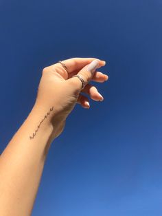 a woman's hand with a small tattoo on her left wrist and the sky in the background