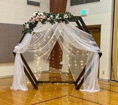 a wedding arch decorated with white flowers and greenery on top of a hard wood floor