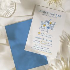 a wedding stationery with two glasses of wine on it and white flowers in the background