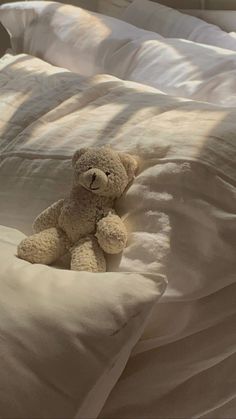 a teddy bear sitting on top of a bed covered in white sheets