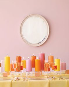 the table is set with many different colored candles and plates on it, along with a round mirror