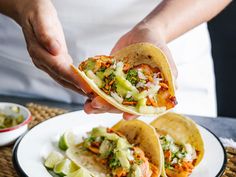 a person is holding up some tacos on a plate