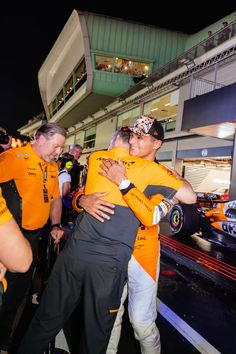 two men hugging each other in front of a race car on the track at night