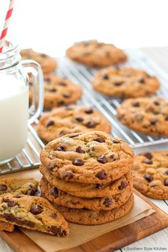 chocolate chip cookies and milk on a wooden cutting board with cooling rack in the background