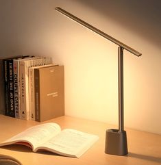 an open book on a desk next to a lamp and some books in front of it