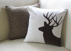 two pillows on a white couch with a deer head drawn on the front and back