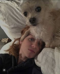 a woman laying in bed with a dog on her head and another dog sitting on top of her