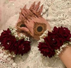 two hands with henna and red flowers on their palms, one holding the other