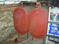 two large red tanks sitting next to each other in a room with exposed pipes and brick walls