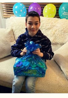 a young boy sitting on a couch holding a blue bag with balloons in the background