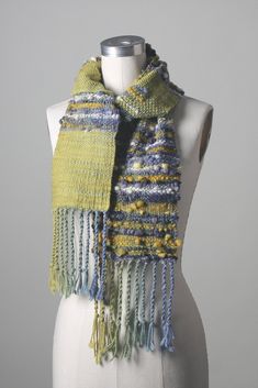 a white mannequin wearing a yellow and blue knitted scarf with fringes