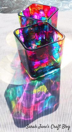 two square glass containers sitting on top of a white tablecloth covered surface with colorful designs