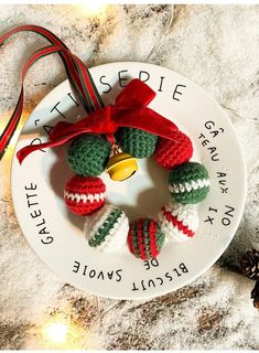 a christmas ornament on a white plate with a red ribbon and pine cones