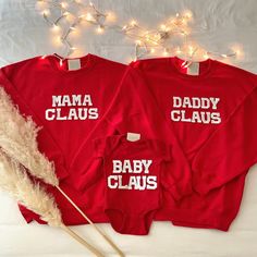 two red sweatshirts with the words mama claus and baby claus printed on them next to a white feather