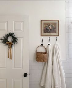 two white towels are hanging on the wall next to a basket with flowers and wreaths