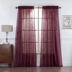 a room with a window and curtains on the windowsill, in front of a wooden dresser