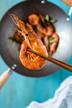 a person holding chopsticks with some shrimp on them in a frying pan