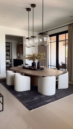 a dining room table with white chairs and lights hanging from it's centerpiece