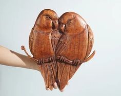 two wooden owls sitting on top of each other's hands, one holding the other