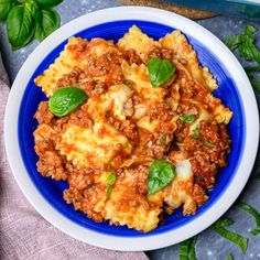 a blue and white plate topped with lasagna covered in meat, cheese and basil