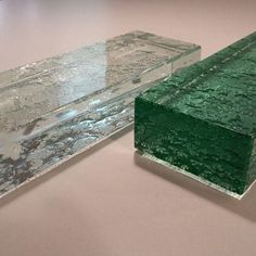 two pieces of green glass sitting on top of a white table next to each other