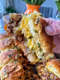 a person holding up a piece of bread with meat and cheese on it in front of other pastries