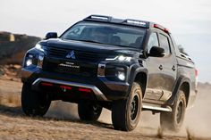 the front end of a black truck driving down a dirt road with words above it